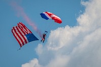 A member of the Patriot Parachute Team drops in with the American Flag in tow to start the afternoon airshow, July 24, 2018.