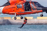 A U.S. Coast Guard rescue swimmer assigned to Air Station Miami jumps out of a, MH-65D Dolphin helicopter to simulate assisting an Airman with the 514th Air Mobility Wing during water survival training at Naval Air Station Key West's Truman Harbor, Key West, Florida, Nov. 16, 2018.