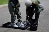 U.S. Air Force Staff Sgt. Stephanie Torres cleans the boots covers of Senior Airman Kimberly Moncayo at the Aircrew Contamination Control Area during an exercise at Joint Base McGuire-Dix-Lakehurst, N.J., June 7, 2017. This image was captured with a tilt-shift lens. Original public domain image from Flickr