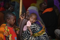 A woman and her children wait to receive food at an Internally Displaced Persons camp at Doolow, Gedo region, Somalia on June 12, 2017. A delegation led by the United Nations and the African Union visited the camp during a humanitarian assessment mission to the Horn of Africa region. UN Photo / Ilyas Ahmed. Original public domain image from Flickr