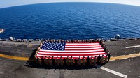 U.S. Marines and Sailors assigned to the 26th Marine Expeditionary Unit (MEU), and Sailors assigned to the USS Kearsarge (LHD 3), hold the American flag to commemorate the Fourth of July during their 2013 deployment on the flight deck of the USS Kearsarge, at sea, July 4, 2013.