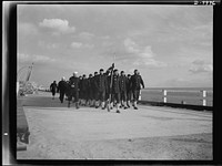 Manhattan Beach Coast Guard training station. On the boardwalk at Manhattan Beach, Company 24, an all African American unit of the Coast Guard training station goes on a hike in zero weather. The company is commanded by coxswain Paul L. Perkins, a former football star at Washington and Jefferson University. Sourced from the Library of Congress.