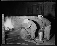 Office of Civilian Defense workers help protect nation's capital. Ever on the alert during patrol, the air raid warden is first to the scene of any action in his sector. Using a wall as a shield from the intense heat, these wardens operate a stirrup pump in extinguishing an incendiary fire during a practice drill in Washington, D.C.. Sourced from the Library of Congress.