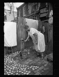 Outside water supply, Washington, D.C. Only source of water supply winter and summer for many houses in slum areas. In some places drainage is so poor that surplus water backs up in huge puddles. Sourced from the Library of Congress.