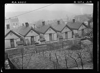 Row of identical houses off Eastern Avenue, in Cincinnati, Ohio, showing backyard outhouses. Ohio River Valley is in the distance. Sourced from the Library of Congress.