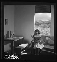 Wife of resettler in her hurricane-proof house, doing needlework (homework for cash income). The furniture was locally built on local materials under P.R.R.A (Puerto Rico Resettlement Administration) guidance. Outside the window a tobacco field and a tobacco barn. La Plata project, Puerto Rico. Sourced from the Library of Congress.