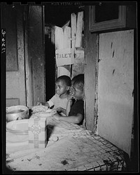 Washington, D.C. Three children waiting in the kitchen while their mother prepares the evening meal. Sourced from the Library of Congress.