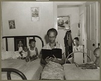 Washington, D.C. Mrs. Ella Watson, a government charwoman, reading the Bible to her household. Sourced from the Library of Congress.