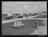 Running water and garbage and refuse disposal cans are placed at head of each shelter unit division at Okeechobee migratory labor camp. Belle Glade, Florida. Sourced from the Library of Congress.