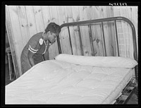 Sidney McLain adjusting the new mattress she made on the bed in her home at La Delta Project. Thomastown, Louisiana. Sourced from the Library of Congress.