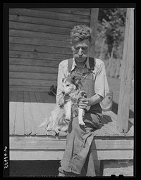 Mountaineer who reared his grandson in his home with the help of the neighbors. He had been crippled with arthritis most of his life. On the steps of a schoolhouse with his dog on South Fork of Kentucky River. Breathitt County, Kentucky. Sourced from the Library of Congress.