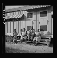 Migratory laborers sitting in front of their metal shelter at Okeechobee migratory labor camp. Belle Glade, Florida. Sourced from the Library of Congress.
