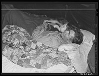 Carpenter and construction worker from Georgia who is recovering from flu.  Next to him is a neighbor's child and his wife is going to take in two other neighbor's children with them because their tent leaks so badly after a week of heavy rains and winds. In this same tent live about ten men, two women and two children.  The men are construction workers sleeping in shifts. Near Camp Livingston, Alexandria, Louisiana. Sourced from the Library of Congress.