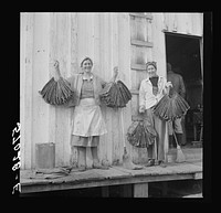 Spanish trapper's wife and sister-in-law holding dried muskrat skins in front of their camp in the marshes near Delacroix Island, Louisiana. Sourced from the Library of Congress.