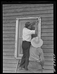 Side strips are nailed over the wire sceen to hold the edges down tightly.  A completed window screen. Screening demonstration. Charles County, La Plata, Maryland. Sourced from the Library of Congress.