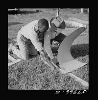 Cutting metal reinforcement strips to fit the screen door joints. Screening demonstration. Saint Mary's County, Ridge, Maryland. Sourced from the Library of Congress.