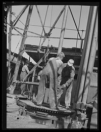 Oil workers pulling up old pipe to change bit on drilling pipe at bottom of oil well in C.C. Graber pool of Continental oil company. Moundridge area near McPherson, Kansas. Sourced from the Library of Congress.