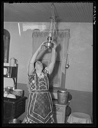 Mrs. Sauer hanging up oil lamp. Cavalier County, North Dakota. Sourced from the Library of Congress.