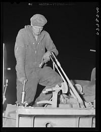 [Untitled photo, possibly related to: Member of road construction gang greasing "cats" at night. Grant County, Wisconsin]. Sourced from the Library of Congress.