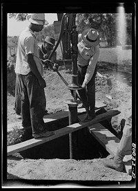 Pump is settled onto pump rod and drop pipe. Pipe wrench still keeps drop pipe from slipping into well. John Fredrick well project, St. Marys County, Maryland. Sourced from the Library of Congress.