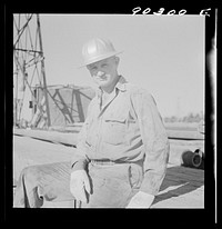 T.J. Schenermann, driller from Oklahoma, worked in Kansas oil fields about fifteen years; by oil well being drilled in Goodrich field of Continental oil field near Wichita, Kansas. Sourced from the Library of Congress.