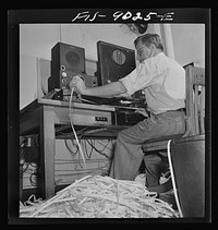 New York, New York. Radio room of the New York Times newspaper. The Times listening post, between 10 and 12 PM, between first and second editions. The operator is listening to Axis news (propaganda) broadcast. Paper in foreground has been previously examined to see what has already been covered in last edition of paper. Operator reports any new angles to city editor. Messages are recorded in tape in international Morse code. Sourced from the Library of Congress.