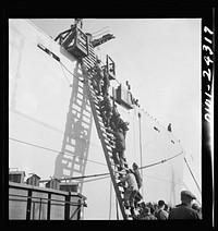 Bethlehem-Fairfield shipyards, Baltimore, Maryland. Workers ascending a ladder at the outfitting pier. Sourced from the Library of Congress.