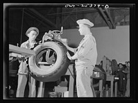 Holabird ordnance depot, Baltimore, Maryland. In the recapping shop, after having been buffed and coated with cement, the tire gets a capping of camelback. It is first put on by hand and then by the power stitcher, as in this picture. Sourced from the Library of Congress.