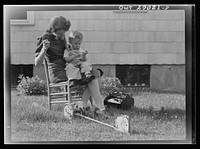 A mother sewing a button on her child's overalls. Silver Spring, Maryland. Sourced from the Library of Congress.