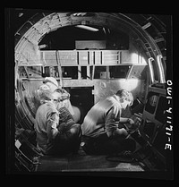 [Untitled photo, possibly related to: Boeing aircraft plant, Seattle, Washington. Production of B-17 (Flying Fortress) bombing planes. A team of men and women workers complete assembly and fitting operations on the interior of a fuselage section]. Sourced from the Library of Congress.