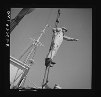 Gloucester, Massachusetts. A lookout climbs the cables high above "Old Glory's" deck to check the location of other trawlers. When one trawler strikes good fishing ground the captain notifies other boats in the fleet. Sourced from the Library of Congress.