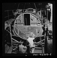 Seattle, Washington. Boeing aircraft plant. Production of B-17F (Flying Fortress) bombing planes. A complete fuselage section is being hoisted from its cradle in rope slings for mating with wing sections. Sourced from the Library of Congress.