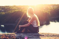 Young blonde woman sitting on rocks overlooking a lake. Original public domain image from Wikimedia Commons