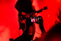 A guitarist performs on stage in red light while an audience member records a concert on their phone. Original public domain image from <a href="https://commons.wikimedia.org/wiki/File:Guitarist_bathed_in_red_light_(Unsplash).jpg" target="_blank" rel="noopener noreferrer nofollow">Wikimedia Commons</a>