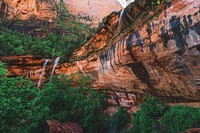 A red rock cliff wall with several small waterfalls coming down from the top. Original public domain image from Wikimedia Commons