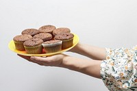 A person holding a tray full of cupcakes. Original public domain image from <a href="https://commons.wikimedia.org/wiki/File:Muffins_on_a_plate_(Unsplash).jpg" target="_blank" rel="noopener noreferrer nofollow">Wikimedia Commons</a>