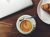 An overhead shot of a latte near a croissant and a MacBook. Original public domain image from Wikimedia Commons