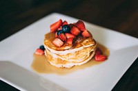 A stack of golden brown pancakes covered in syrup and fresh strawberries and blueberries on a white plate. Original public domain image from Wikimedia Commons