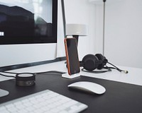 An iPhone near a pair of headphones and a small speaker on a computer desk. Original public domain image from Wikimedia Commons