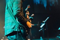 A musician in a plaid shirt playing a black electric guitar during a concert. Original public domain image from Wikimedia Commons