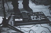 A low black-and-white shot of music equipment next to a person's shoes on stage. Original public domain image from Wikimedia Commons