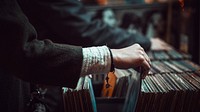 A close-up of the hand of a person browsing vinyl records at a store. Original public domain image from <a href="https://commons.wikimedia.org/wiki/File:Browsing_record_store_shelves_(Unsplash).jpg" target="_blank" rel="noopener noreferrer nofollow">Wikimedia Commons</a>