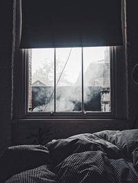 Interior of a bedroom with a blanket and a window showing smoke and other houses outside. Original public domain image from <a href="https://commons.wikimedia.org/wiki/File:Bedroom_window_(Unsplash).jpg" target="_blank" rel="noopener noreferrer nofollow">Wikimedia Commons</a>