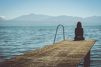 A girl in Morges sits at the end of a dock and stares at the mountains. Original public domain image from Wikimedia Commons