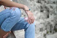 A seated woman in jeans with a bracelet on her wrist. Original public domain image from Wikimedia Commons
