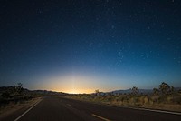The pavement in the center of desert area leads to glowing sunrise illuminating night sky. Original public domain image from Wikimedia Commons