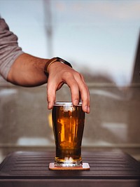 A man with a rolled up sleeve holding the tip of a glass cup of beer, relaxing. Original public domain image from <a href="https://commons.wikimedia.org/wiki/File:Man_holding_glass_of_beer_(Unsplash).jpg" target="_blank" rel="noopener noreferrer nofollow">Wikimedia Commons</a>