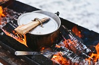 A metal pot sitting in a wood firepit with a log used to pick up the hot lid. Original public domain image from Wikimedia Commons