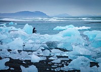 A photographer setting up a camera on a tripod on melting blue glaciers in the ocean. Original public domain image from <a href="https://commons.wikimedia.org/wiki/File:At_the_seaside_(Unsplash).jpg" target="_blank" rel="noopener noreferrer nofollow">Wikimedia Commons</a>