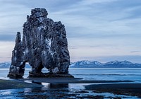 Tall rock formation above the ocean with snow covered mountains in the background at Hvítserkur. Original public domain image from Wikimedia Commons